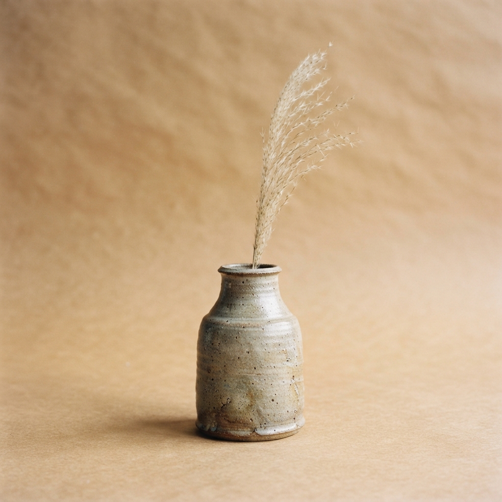 Speckled ceramic vase holding pale dried grasses on a warm beige background.
